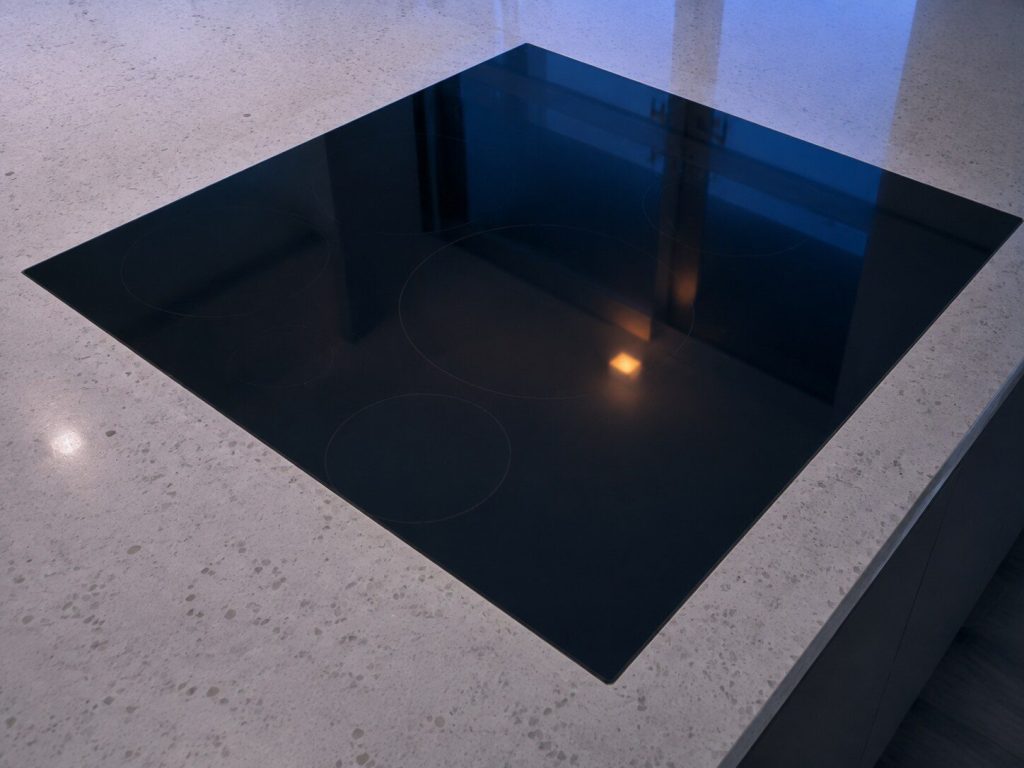 "A black glass induction cooktop set flush into a quartz counter ... the ring outlines are only just visible in the reflection" — a glass top dropped into a counter, unlit and dark, and induction is one of the three types this page covers