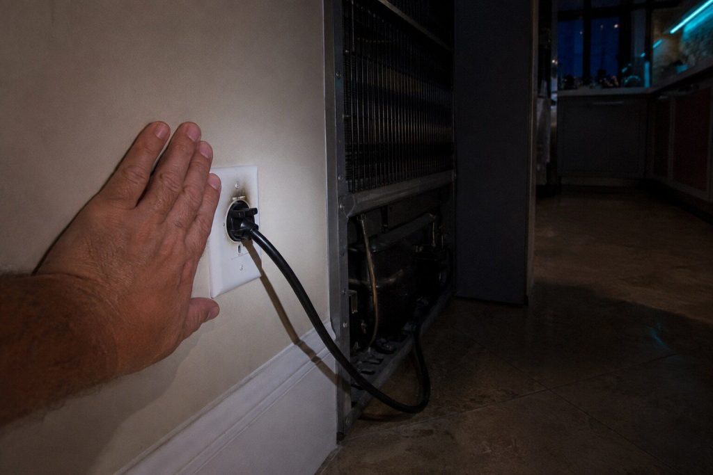 "The back of a hand held against the faceplate of a wall outlet behind an appliance pulled out from the wall, the plug seated in the socket beside it, a scorch shadow on the plate" — the first minute of this page, exactly