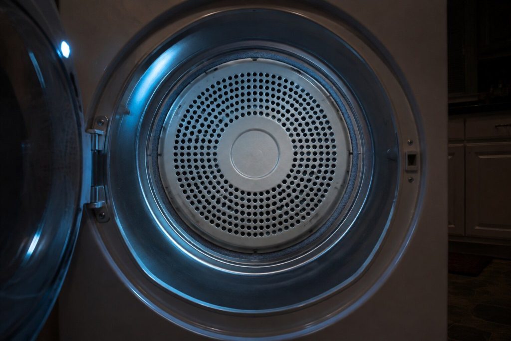 The rear bulkhead at the back of an empty dryer drum seen through the open door: its ring of small air holes, the felt seal round the rim and the smooth drum wall curving away either side.