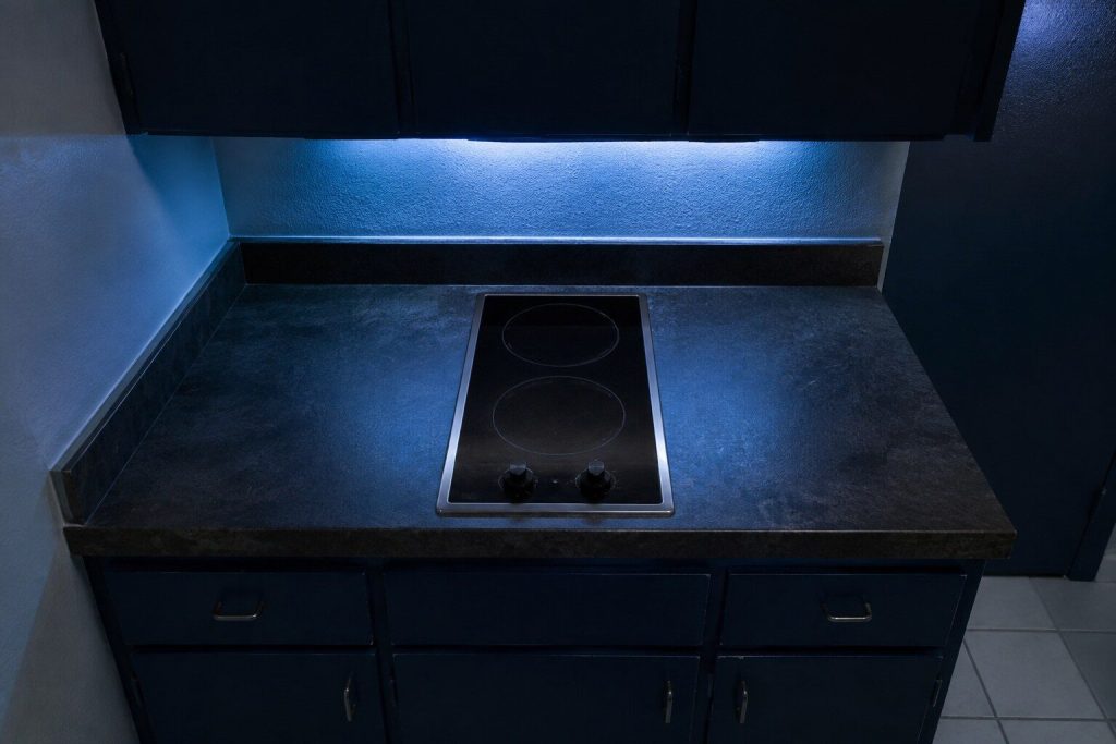 A very small drop-in electric cooktop carrying only TWO ceramic element rings, one behind the other, set into a short strip of laminate counter in a small apartment kitchen — about half the width of an ordinary four-zone cooktop, with counter surface either side of it for scale.