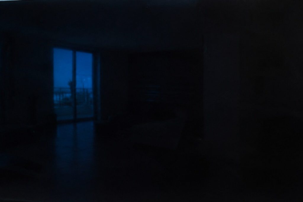 The black glass face of a control panel filling the whole frame, unlit, carrying only a soft reflection of a window.