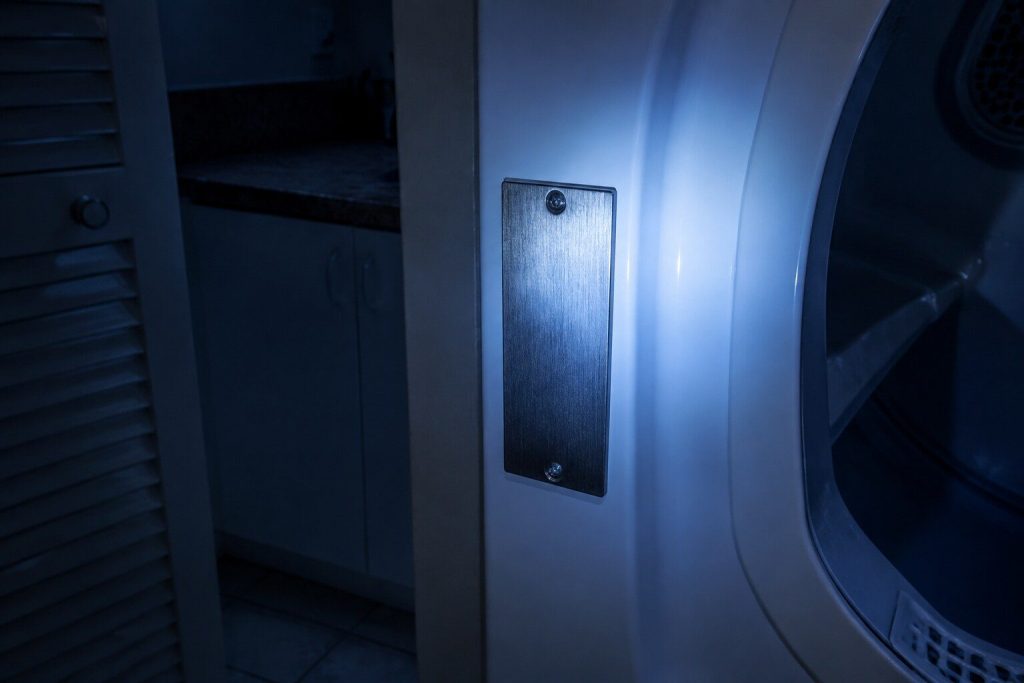 A blank metal rating plate on the inner frame of a machine's door recess, lit by a torch held just out of frame.