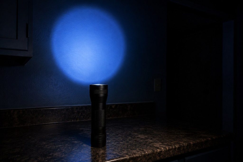 A torch standing upright on end on a dark counter throwing a circle of light up onto the wall behind it, the rest of the room black.