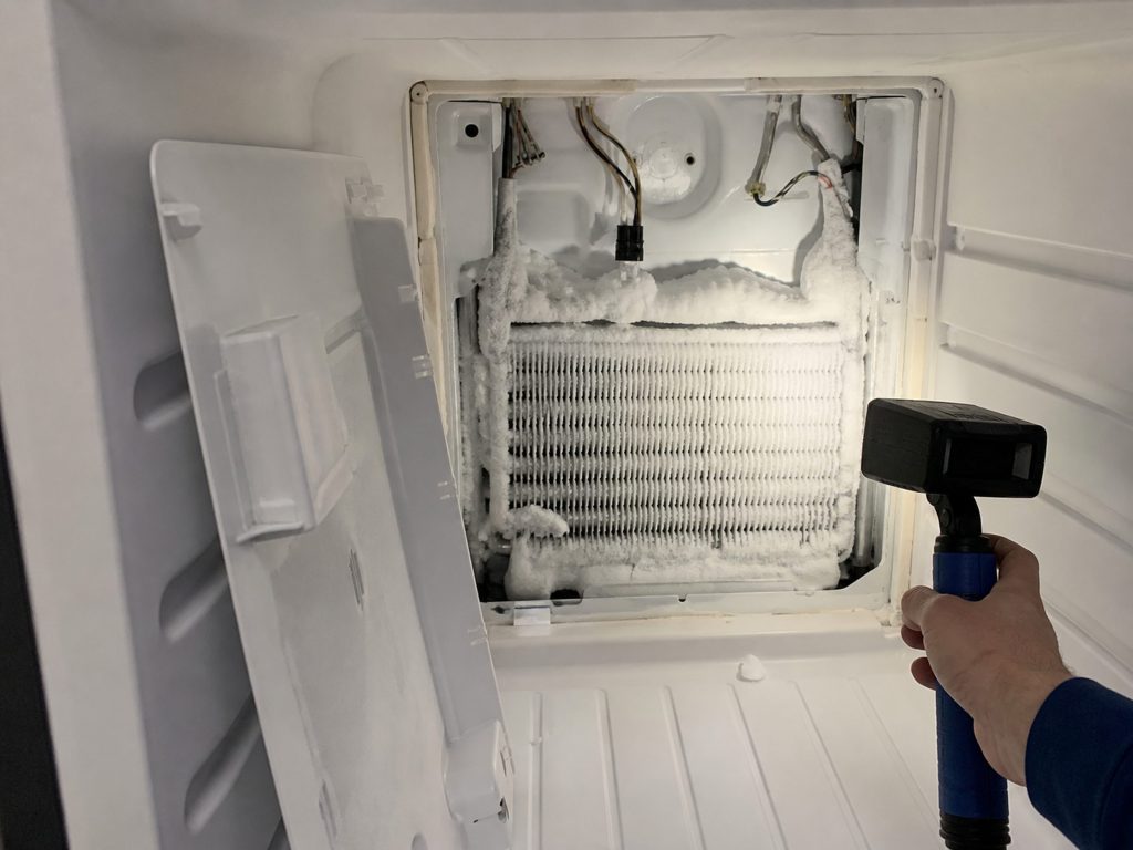 "The rear panel of a freezer compartment removed and leaning aside, the evaporator coil behind it thick with white frost, a work light across it" — the frame is the inside of a freezer wall under a work light, which carries no palette of its own