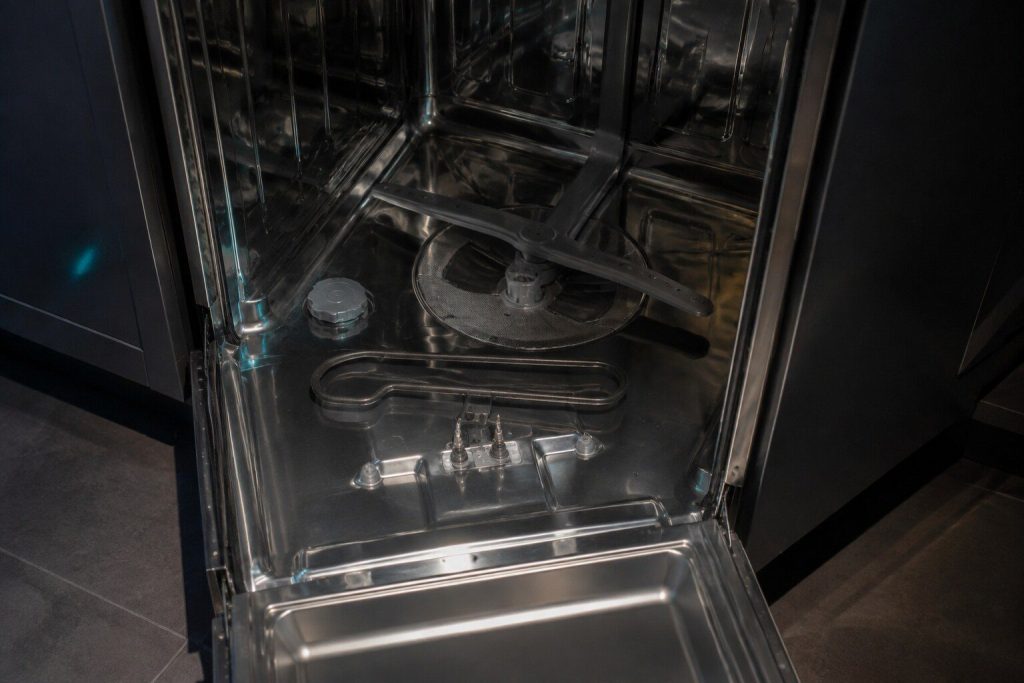 "The looped heating element lifted a little clear of the floor of a dishwasher tub with the lower rack out, its two terminals visible where they pass through the base"