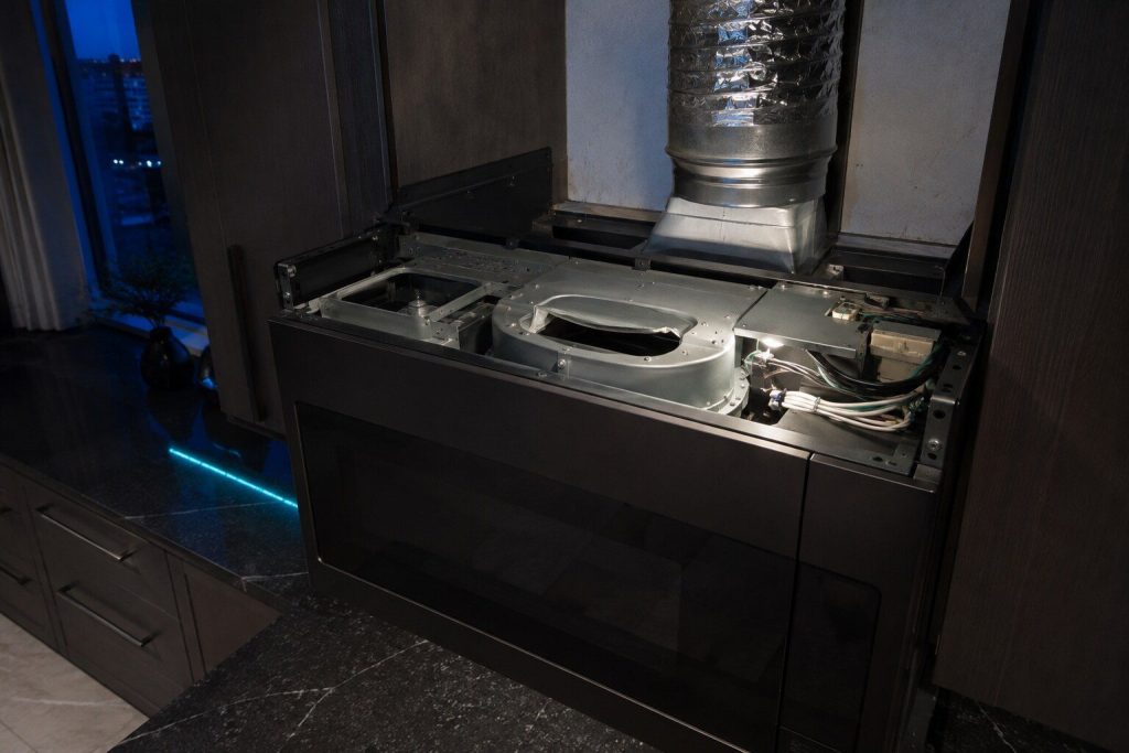 "The blower housing inside the top of an over-the-range microwave with its vent flap turned to the other setting, the top cover removed and the ductwork above visible" — recirculating against ducted, which is the condominium question